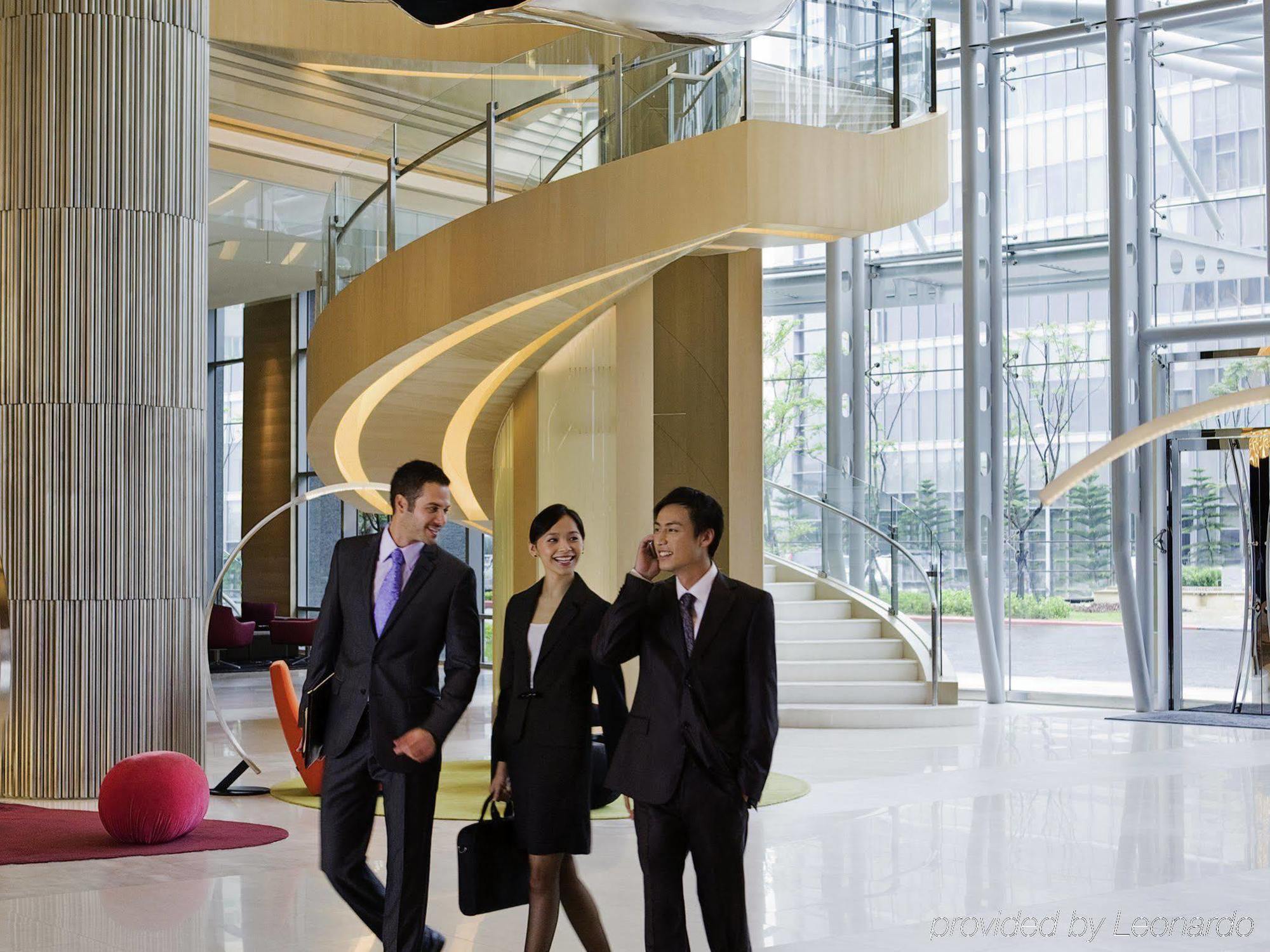 Готель Hyatt Regency Taoyuan International Airport Екстер'єр фото The photo depicts a modern and elegantly designed lobby area with a large, spiraling staircase in the background. Three individuals are walking together, dressed in formal business attire. The setting features large glass windows that allow natural l